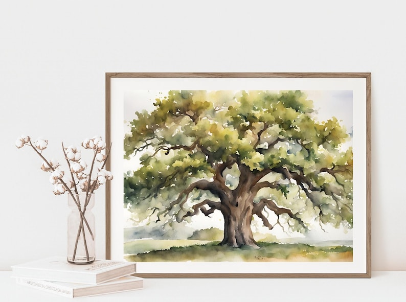 May include: Watercolor painting of a large oak tree with sprawling branches and lush green foliage. The artwork is framed in a light brown wooden frame. The painting is displayed on a white surface with books and a vase of flowers.