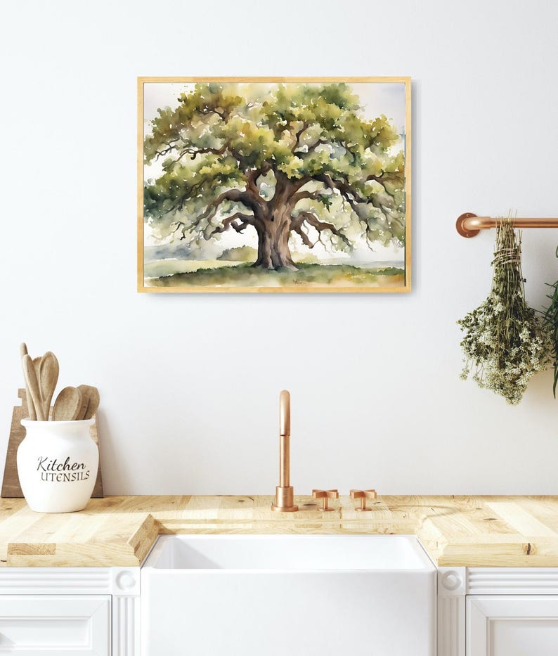 May include: Watercolor painting of a large oak tree with a wide canopy and a thick trunk. The artwork is framed in a light wood frame. The painting has green, brown, and yellow hues. The artwork is displayed above a white sink in a kitchen.