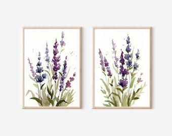 May include: Two watercolor paintings of lavender flowers in shades of purple and green. The paintings are framed in natural wood frames and are displayed on a white wall.
