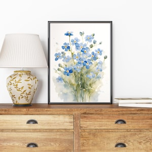 May include: A framed watercolour painting of a bouquet of blue forget-me-not flowers with green stems and leaves. The flowers are painted in a realistic style with delicate brushstrokes.