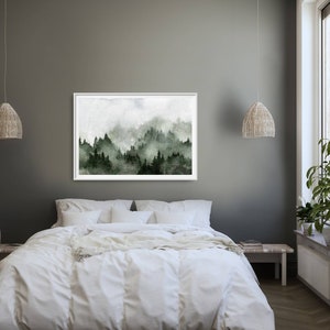 May include: A framed watercolour painting of a misty forest scene with green trees and a white background. The painting is hanging on a grey wall above a white bed with white bedding.