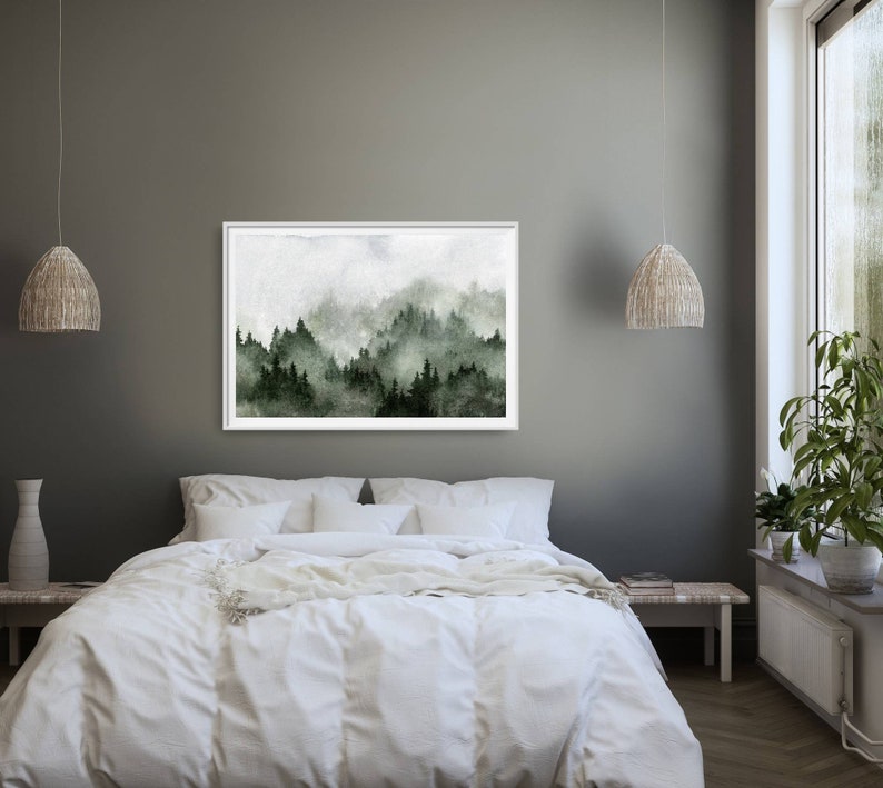 May include: A framed watercolour painting of a misty forest scene with green trees and a white background. The painting is hanging on a grey wall above a white bed with white bedding.