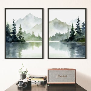 May include: Two framed watercolor paintings of a misty mountain lake scene with green trees and a reflection of the mountains in the water.