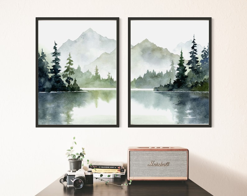May include: Two framed watercolor paintings of a misty mountain lake scene with green trees and a reflection of the mountains in the water.