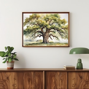 May include: A framed watercolor painting of a large oak tree with lush green foliage and a thick, textured trunk. The artwork is displayed on a white wall above a wooden cabinet, with a green lamp and potted plant in the foreground.