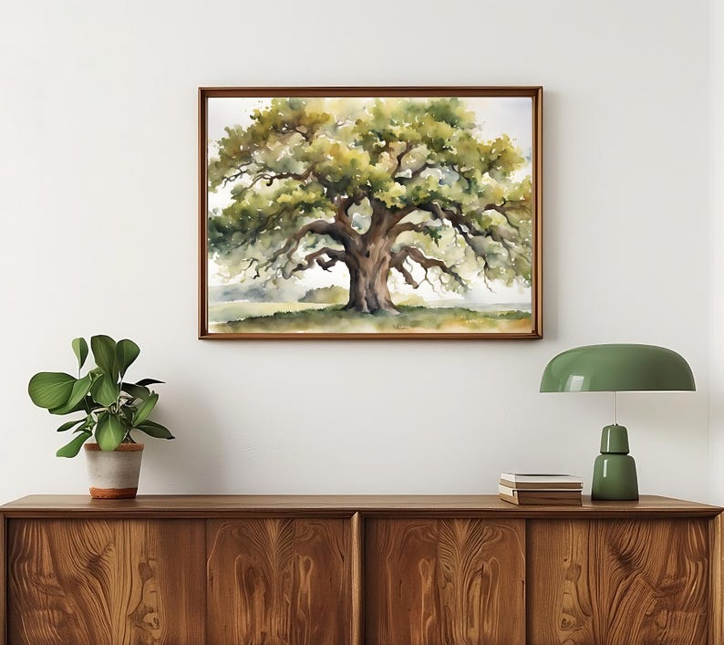 May include: A framed watercolor painting of a large oak tree with lush green foliage and a thick, textured trunk. The artwork is displayed on a white wall above a wooden cabinet, with a green lamp and potted plant in the foreground.