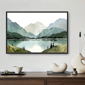 May include: A watercolor painting of a mountain range with a lake in the foreground. The mountains are painted in shades of green and blue, and the lake is a light blue. The painting is framed in a black frame.