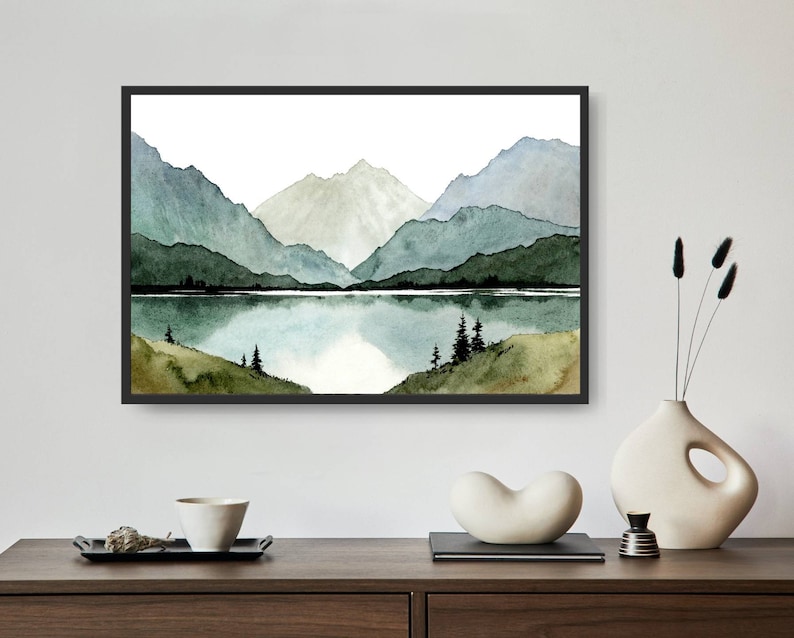 May include: A watercolor painting of a mountain range with a lake in the foreground. The mountains are painted in shades of green and blue, and the lake is a light blue. The painting is framed in a black frame.