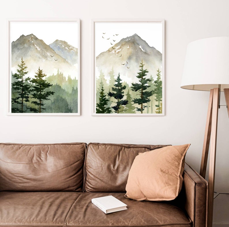 Puede incluir: Dos acuarelas de una cordillera monta&ntilde;osa con un bosque en primer plano. Las pinturas est&aacute;n enmarcadas en blanco y est&aacute;n colgadas en una pared blanca. Las pinturas est&aacute;n en un sal&oacute;n con un sof&aacute; de cuero marr&oacute;n y un coj&iacute;n marr&oacute;n.