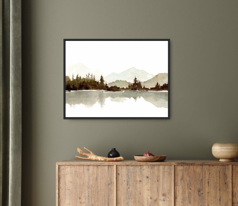 May include: A watercolour painting of a mountain range reflected in a lake. The mountains are a light brown colour and the lake is a light blue colour. The trees are a dark green colour and are silhouetted against the mountains.