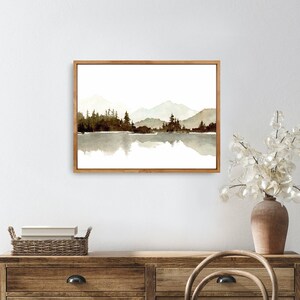 May include: A watercolour painting of a mountain range reflected in a still lake. The mountains are a light brown colour and the lake is a dark brown colour. The painting is framed in a light wood frame.