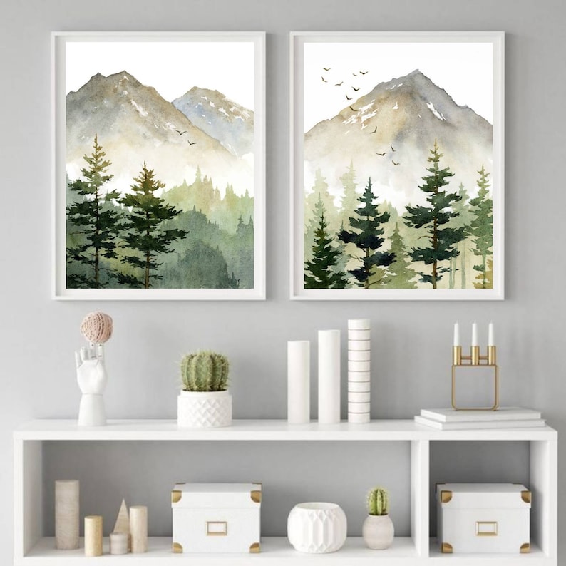 Puede incluir: Dos acuarelas de una cordillera monta&ntilde;osa con un bosque en primer plano. Las pinturas est&aacute;n enmarcadas en blanco y colgadas en una pared gris sobre una estanter&iacute;a blanca con art&iacute;culos decorativos.
