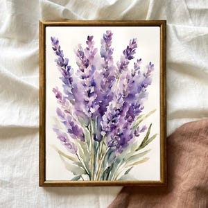 May include: A framed watercolour painting of lavender flowers. The artwork features a bouquet of purple lavender blossoms with green leaves, set against a white background. The frame is a warm gold colour.
