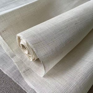 May include: A close-up of a roll of white fabric. The fabric is woven with a fine, even texture and has a slightly rough surface.