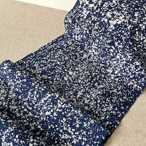 May include: A close-up of a blue fabric with white splatter paint. The fabric has a speckled appearance and is folded in half.