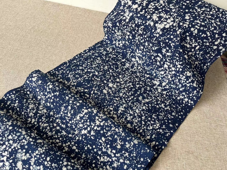 May include: A close-up of a blue fabric with white splatter paint. The fabric has a speckled appearance and is folded in half.
