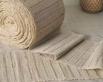 May include: A roll of natural fiber rug material, woven with a striped pattern. The material is unraveled and laid out flat, showing the texture and weave.