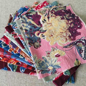 May include: A stack of fabric squares with floral and butterfly patterns in shades of pink, blue, red, and green.