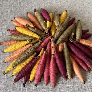 May include: A collection of colourful spools of thread, with shades of yellow, orange, red, and green. The spools are arranged in a circular pattern, with the ends of the thread extending outward.