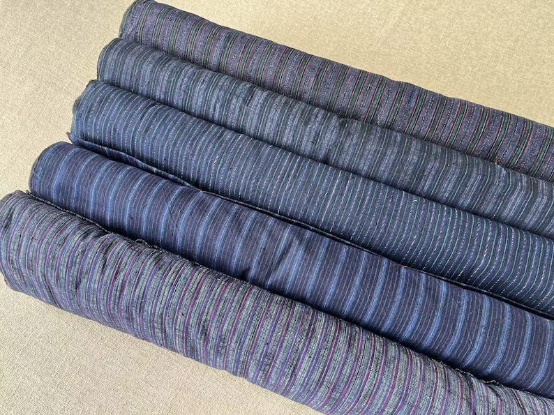 May include: A stack of five fabric rolls with a striped pattern in shades of blue, gray, and purple.