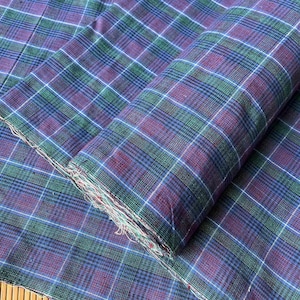 Puede incluir: Un primer plano de una tela de cuadros azules y verdes. La tela está doblada por la mitad y el patrón de cuadros es visible en ambos lados.