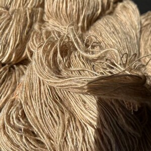 May include: A close-up of a skein of beige yarn. The yarn is soft and fluffy, and it has a subtle sheen.