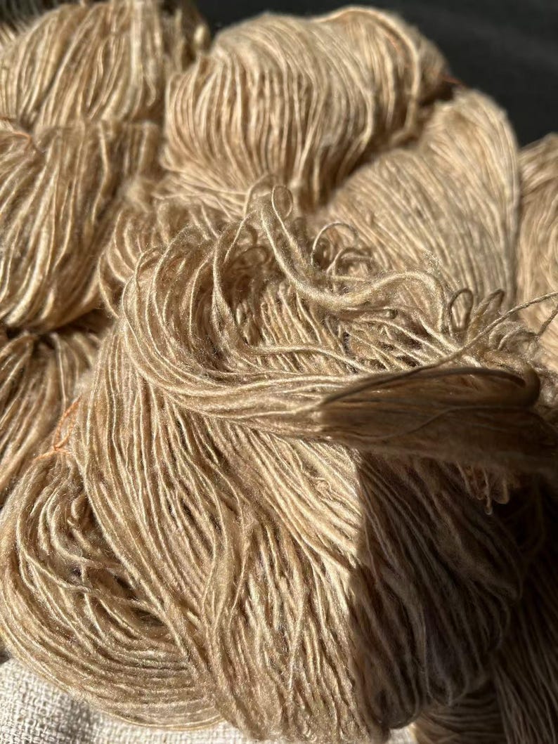 May include: A close-up of a skein of beige yarn. The yarn is soft and fluffy, and it has a subtle sheen.