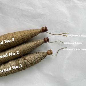May include: Three spools of thread labeled Thread No. 1, 2, and 3. The thread is a natural tan color, with wooden ends. The thickness of the thread is labeled as 0.8mm, 0.5mm, and 0.6-0.7mm.