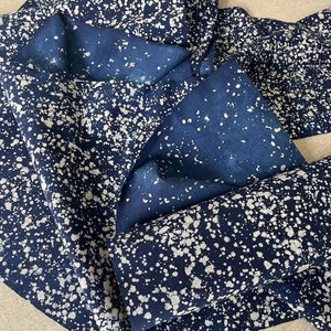 May include: A close-up of a blue fabric with white splatter paint. The fabric is folded and shows the pattern on both sides.