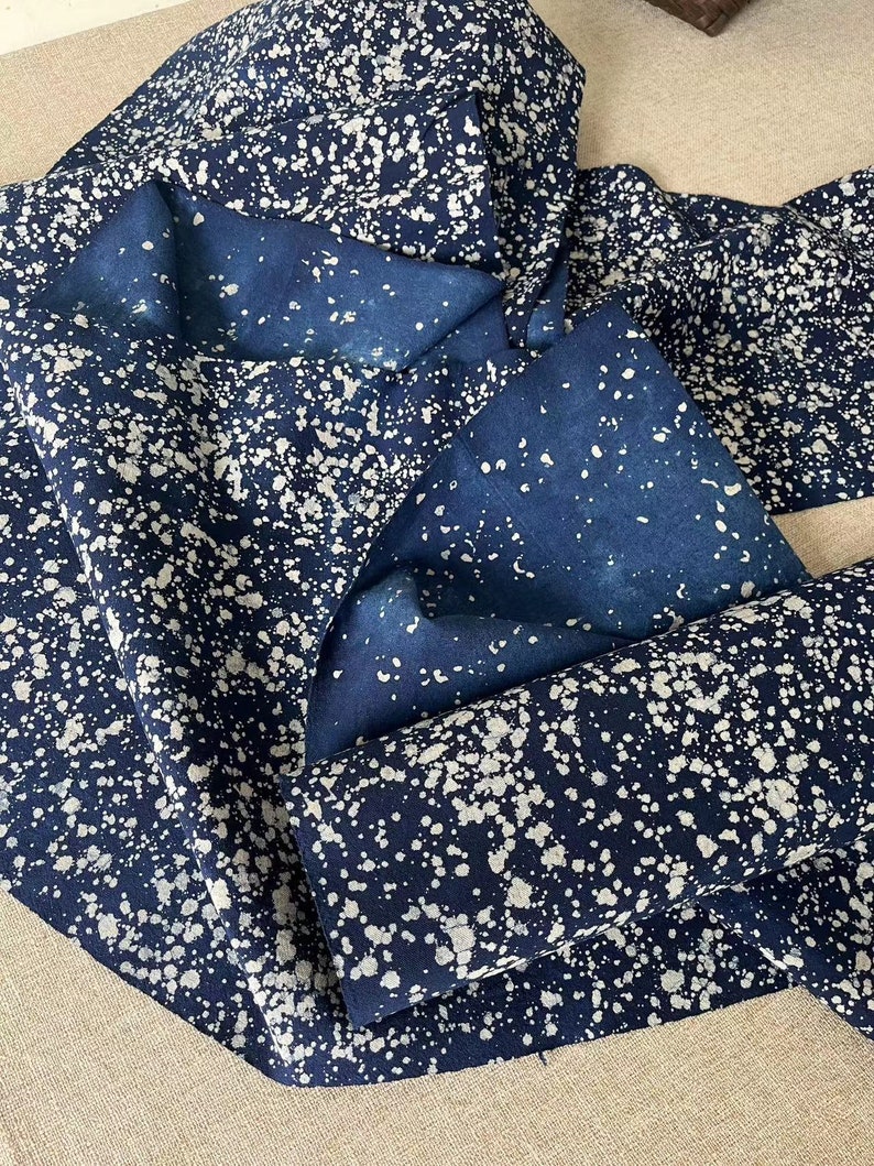 May include: A close-up of a blue fabric with white splatter paint. The fabric is folded and shows the pattern on both sides.