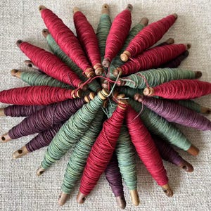 May include: A collection of spools of thread in shades of red, green, and purple. The spools are arranged in a circular pattern, with the ends of the thread extending outward.