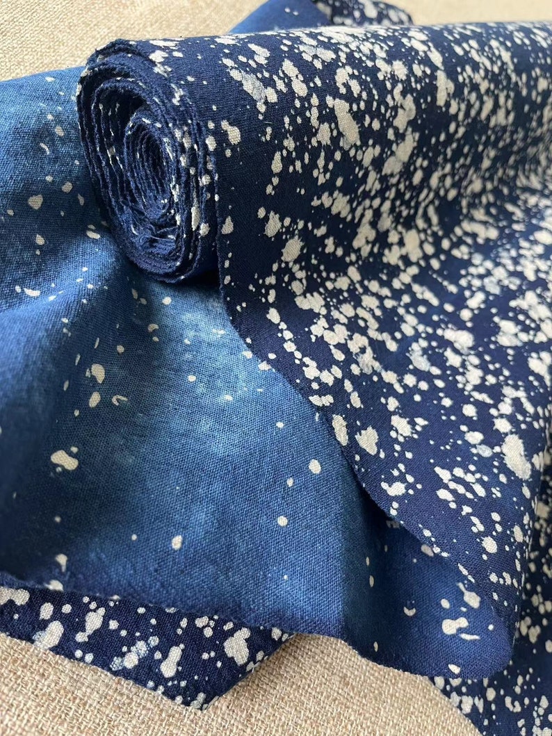 May include: A roll of blue fabric with white splatter paint. The fabric is folded in half and the roll is partially unrolled.