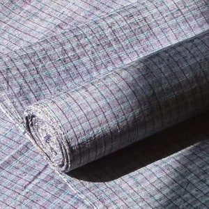 May include: A roll of gray and white checkered fabric with a subtle blue hue. The fabric is woven with a fine texture and has a slightly rough feel.