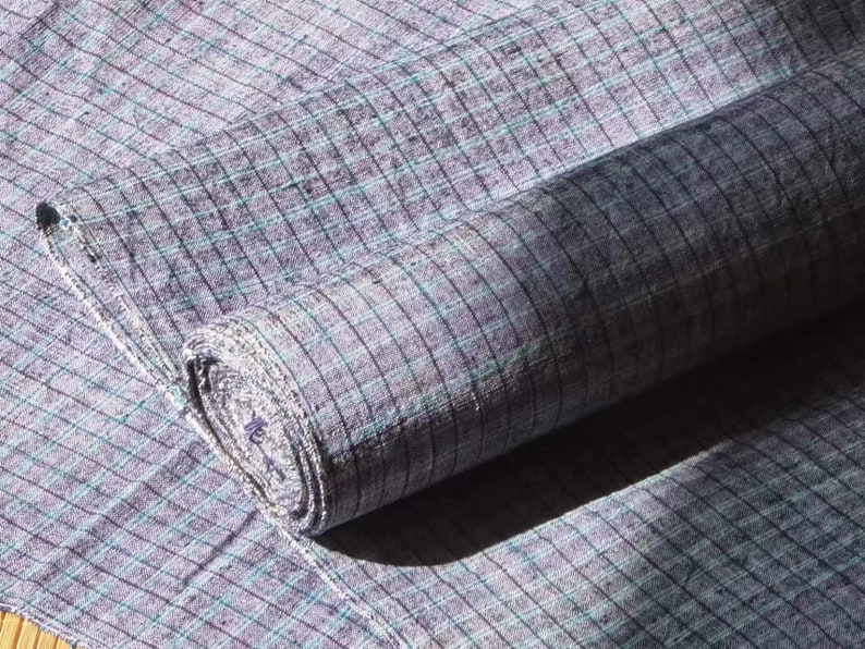 May include: A roll of gray and white checkered fabric with a subtle blue hue. The fabric is woven with a fine texture and has a slightly rough feel.
