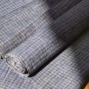 May include: A roll of gray and green plaid fabric with a subtle sheen. The fabric is folded and rolled up, with the ends of the fabric visible.