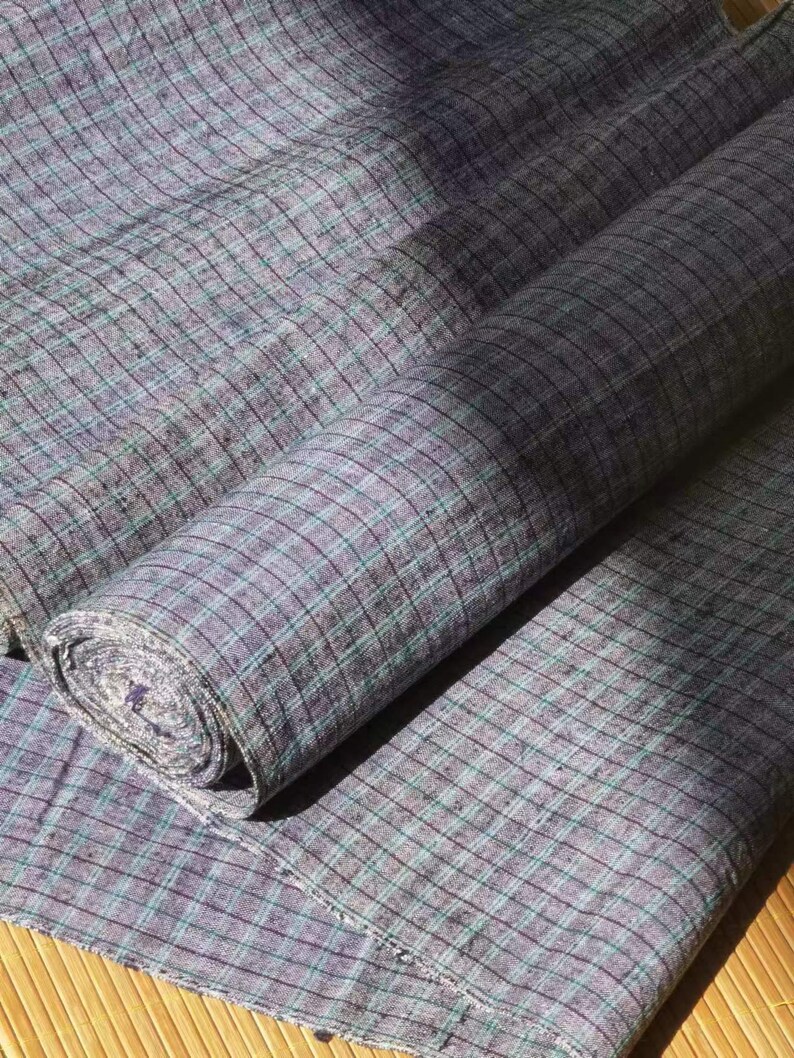 May include: A roll of gray and green plaid fabric with a subtle sheen. The fabric is folded and rolled up, with the ends of the fabric visible.