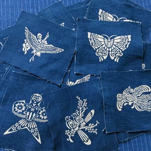 Puede incluir: Una pila de cuadrados de tela azul con diseños blancos de pájaros, mariposas y flores. Los cuadrados de tela son todos del mismo tamaño y están dispuestos en un orden aleatorio.