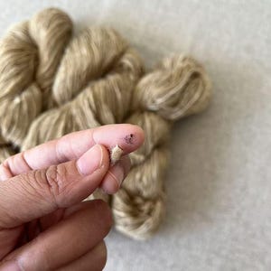 May include: Close-up of a skein of beige yarn with a few strands pulled out. The yarn is soft and fluffy, and it has a subtle sheen.