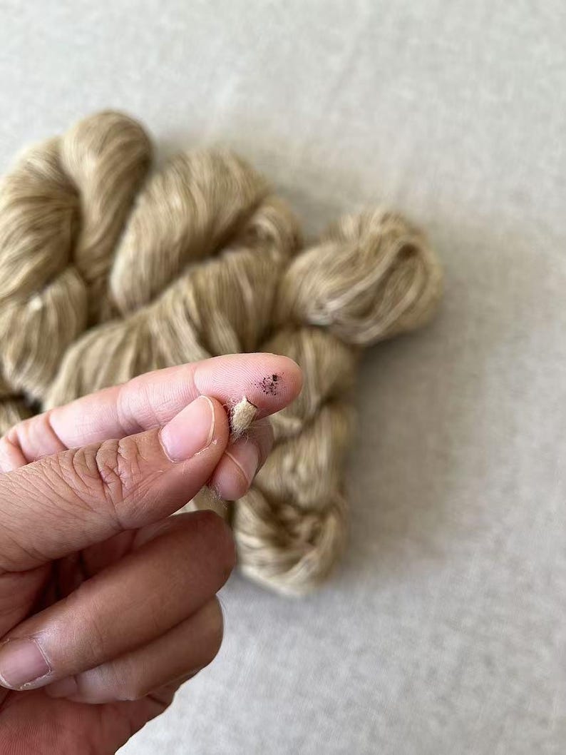 May include: Close-up of a skein of beige yarn with a few strands pulled out. The yarn is soft and fluffy, and it has a subtle sheen.