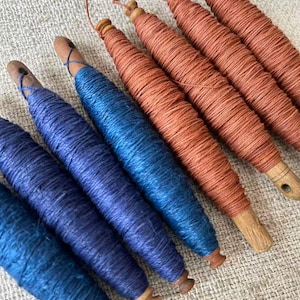 May include: A collection of wooden spools wrapped with vibrant blue and orange thread. The spools have a natural wood finish and are arranged diagonally, showcasing the colorful thread. The thread is tightly wound, creating a textured appearance.