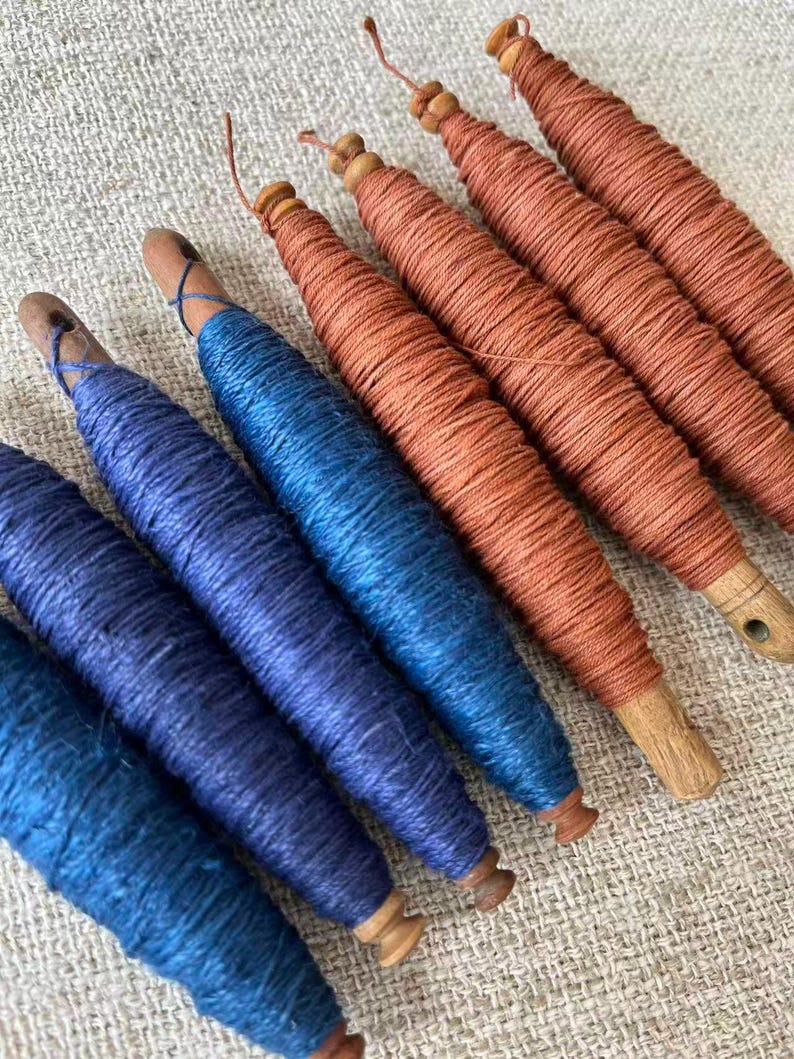 May include: A collection of wooden spools wrapped with vibrant blue and orange thread. The spools have a natural wood finish and are arranged diagonally, showcasing the colorful thread. The thread is tightly wound, creating a textured appearance.