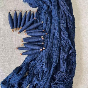 K&ouml;nnte beinhalten: Ein gro&szlig;er Stapel tiefblauer Wolle mit Holzspulen aus der gleichen Wolle.