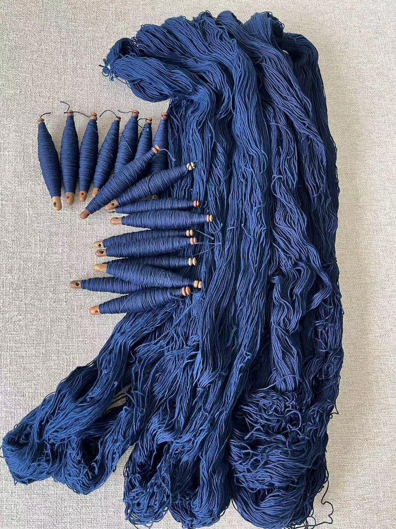 K&ouml;nnte beinhalten: Ein gro&szlig;er Stapel tiefblauer Wolle mit Holzspulen aus der gleichen Wolle.