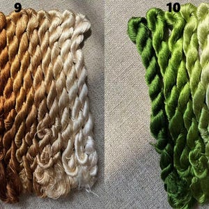 Pode incluir: Dois conjuntos de fio de bordado, um conjunto em tons de marrom e bege, e o outro em tons de verde e branco. O fio &eacute; organizado em feixes, cada feixe cont&eacute;m v&aacute;rios fios de fio.