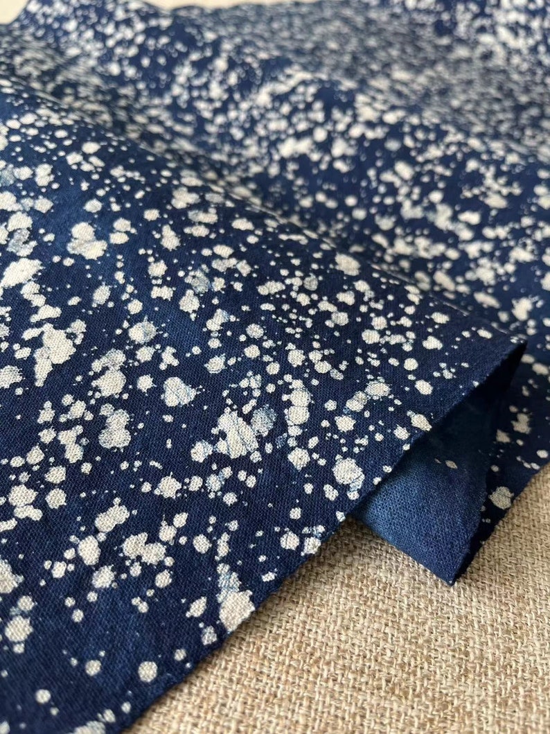 May include: A close-up of a dark blue fabric with a white splatter pattern. The fabric is folded over and the edges are visible.