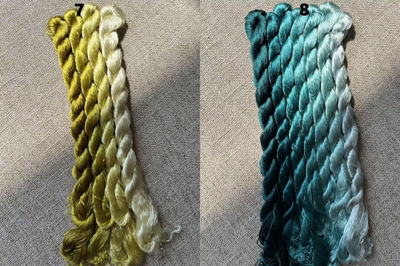 Pode incluir: Dois conjuntos de fio para bordar, um em tons de verde e amarelo, e o outro em tons de azul-esverdeado e azul. O fio est&aacute; disposto em um padr&atilde;o de degrad&ecirc;, com os tons mais escuros na parte inferior e os tons mais claros na parte superior. O fio est&aacute; etiquetado com os n&uacute;meros 7 e 8.