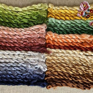 Pode incluir: Uma cole&ccedil;&atilde;o de carret&eacute;is de fio de bordado em v&aacute;rias cores, incluindo verde, rosa, vermelho, branco, azul e marrom. O fio est&aacute; disposto em filas, com cada fila contendo uma cor diferente. O fio &eacute; torcido e texturizado, criando uma exibi&ccedil;&atilde;o visualmente atraente.