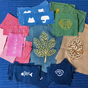 May include: A collection of fabric squares with various designs and text in Japanese. The squares are in shades of blue, green, brown, pink, and white. The designs include a cat, an elephant, a leaf, a fish, and a cloud. The text includes the words "miss you" and Japanese characters.