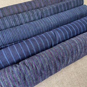 May include: Four rolls of blue and white striped fabric with a subtle sheen. The fabric has a woven texture and is likely cotton.