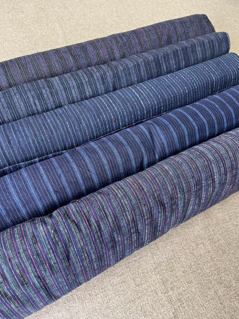 May include: Four rolls of blue and white striped fabric with a subtle sheen. The fabric has a woven texture and is likely cotton.